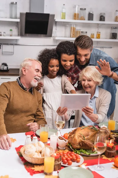 Concentration sélective de la famille multiethnique ayant le chat vidéo sur la tablette numérique près de la dinde pendant l'Action de grâces — Photo de stock