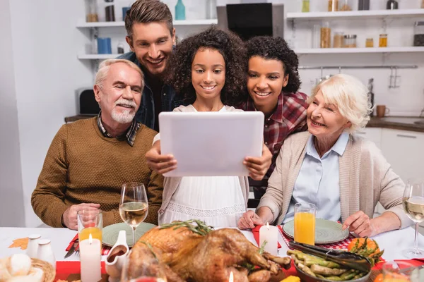 Selective focus of african american girl holding digital tablet near parents during thanksgiving celebration — Stock Photo