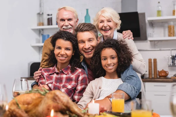 Enfoque selectivo de la familia multicultural mirando a la cámara mientras celebra el Día de Acción de Gracias - foto de stock