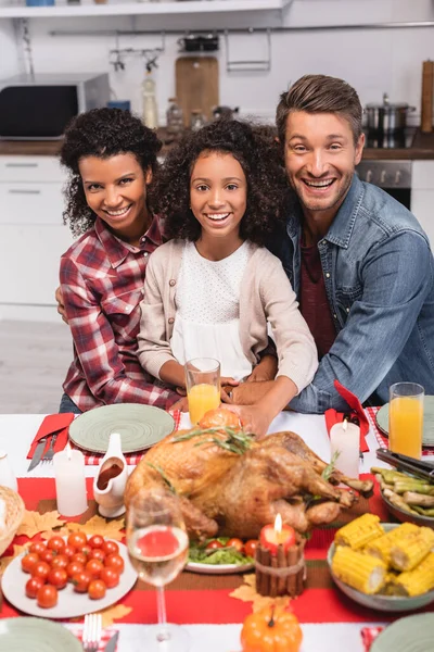 Селективный фокус многонациональных родителей, обнимающих африканского американского ребенка возле еды во время Дня Благодарения — стоковое фото