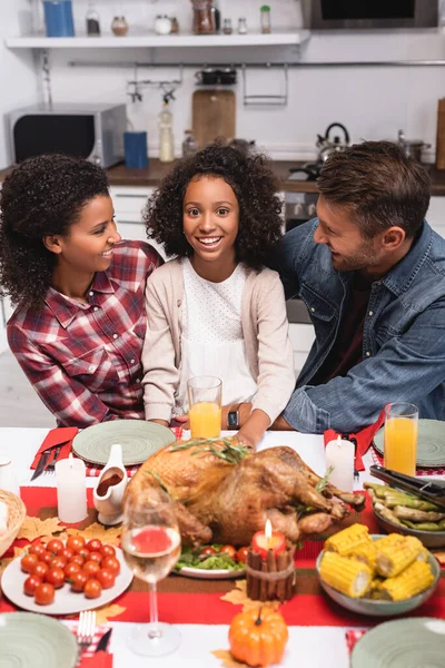 Enfoque selectivo de los padres multiétnicos que miran a la hija afroamericana durante el Día de Acción de Gracias en casa - foto de stock