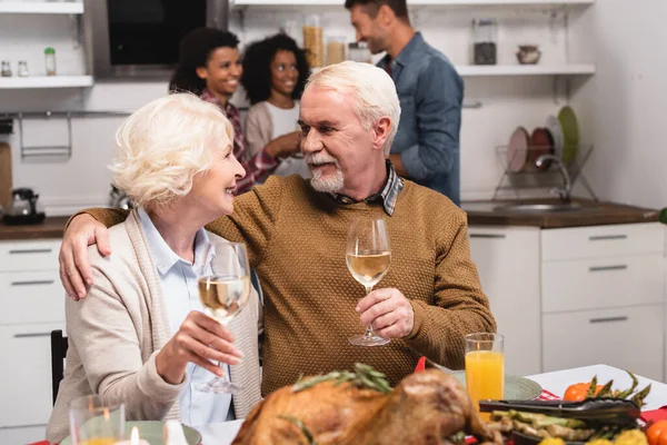 Enfoque selectivo del hombre mayor abrazando a la esposa durante la celebración de acción de gracias con la familia multiétnica - foto de stock