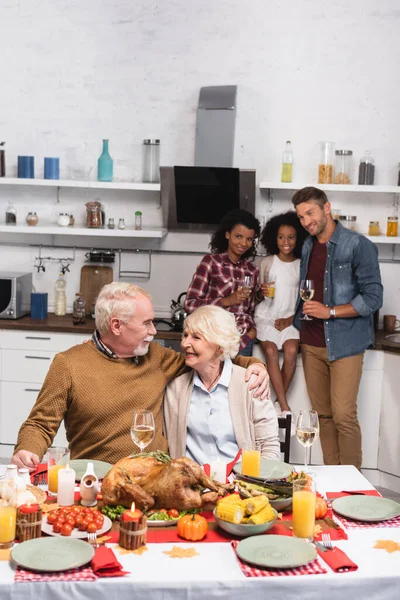 Selektiver Fokus eines älteren Mannes, der seine Frau ansieht, während er mit multiethnischer Familie Erntedank feiert — Stockfoto