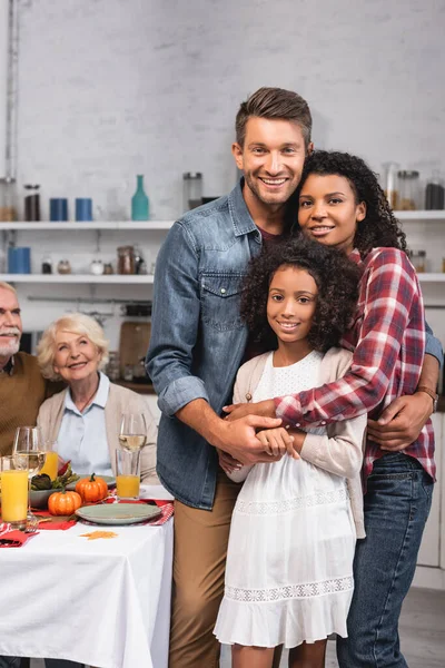 Selektiver Fokus der Eltern, die ihre afrikanisch-amerikanische Tochter während des Erntedankfestes in der Nähe des Essens auf dem Tisch umarmen — Stockfoto