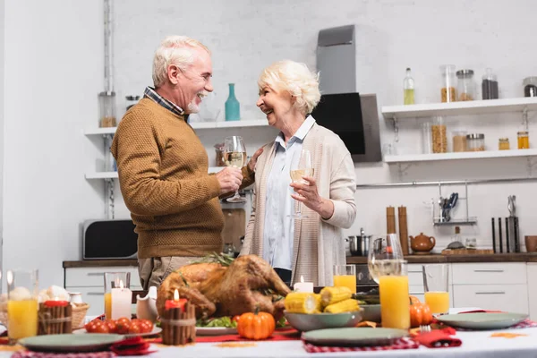 Selective focus of elderly couple with glass of wine celebrating thanksgiving near food on table — Stock Photo