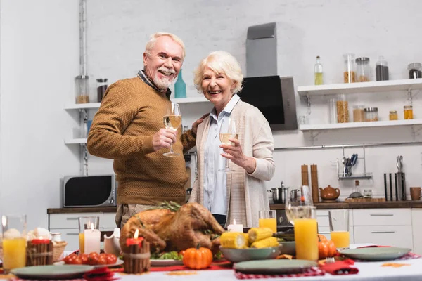 Focus selettivo della coppia anziana con bicchieri di vino guardando la fotocamera vicino al tacchino e le candele sul tavolo — Foto stock