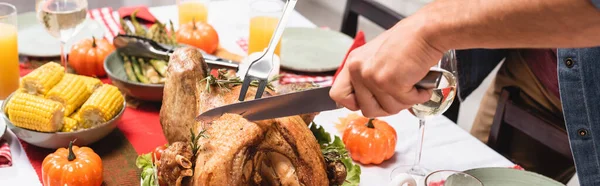 Horizontal crop of man cutting turkey near decorations during thanksgiving dinner — Stock Photo