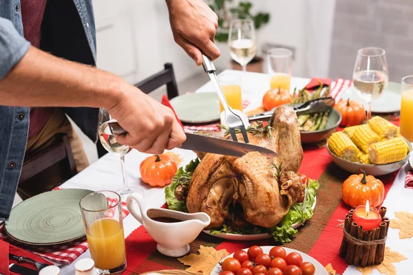 Ausgeschnittene Ansicht eines Mannes, der Truthahn in der Nähe von Erntedank-Dekorationen auf dem Tisch schneidet — Stockfoto