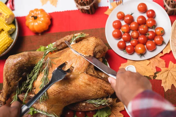 Cropped view of african american woman with fork and knife cutting turkey during thanksgiving dinner — Stock Photo