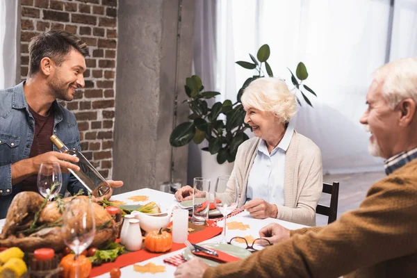 Селективный фокус человека, держащего бутылку вина рядом с пожилыми родителями во время празднования Дня благодарения — стоковое фото