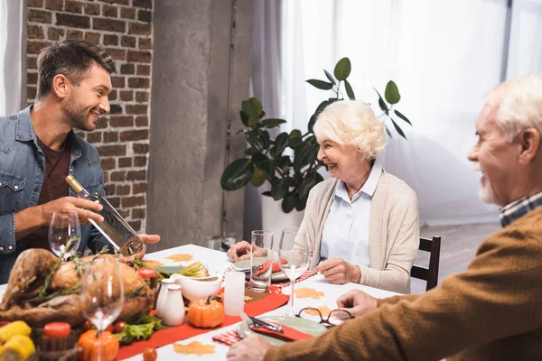 Focus selettivo dell'uomo che tiene una bottiglia di vino vicino ai genitori anziani durante la celebrazione del Ringraziamento — Foto stock