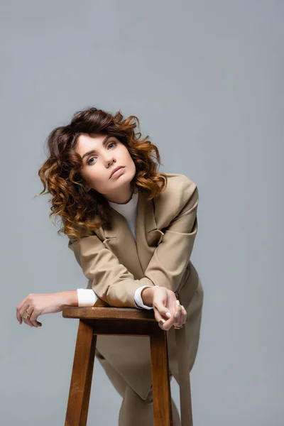 Elegant woman in beige suit posing on wooden chair isolated on grey — Stock Photo