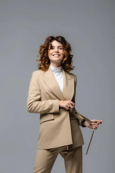 Elegante donna in abito beige in posa e sorridente isolata sul grigio — Foto stock