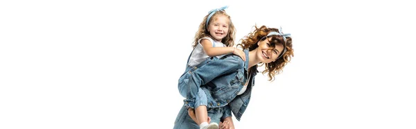 Vista laterale di ridere madre piggybacking figlia in denim vestito isolato su bianco, colpo panoramico — Foto stock