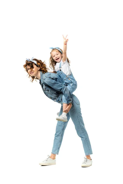 Side view of laughing mother piggybacking daughter in denim outfit isolated on white — Stock Photo