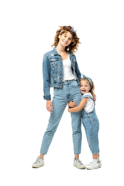 Hija en traje de mezclilla abrazando la pierna madre aislada en blanco - foto de stock