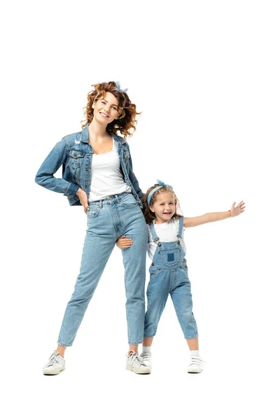 Дочка в джинсовому вбранні, обіймаючи матір'ю ногу з витягнутою рукою ізольовано на білому — стокове фото
