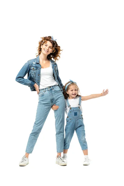 Hija en traje de mezclilla abrazando la pierna madre con la mano extendida aislada en blanco - foto de stock