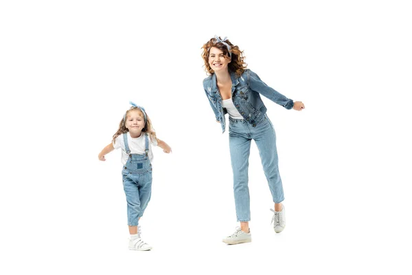 Madre e hija en trajes de mezclilla posando y sonriendo aisladas en blanco - foto de stock