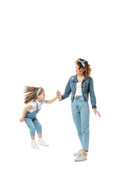 Hija en traje de mezclilla saltando y aplaudiendo con la madre aislada en blanco - foto de stock