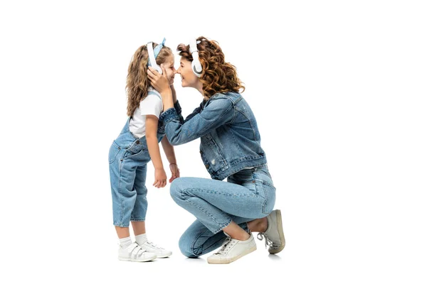 Seitenansicht von Mutter und Tochter in Jeans-Outfits, die mit Kopfhörern Musik hören, von Angesicht zu Angesicht isoliert auf weiß — Stockfoto