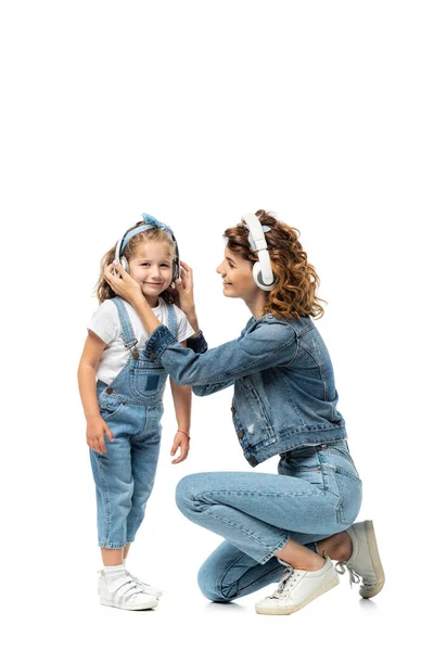 Madre e hija en trajes de mezclilla escuchando música en auriculares aislados en blanco - foto de stock