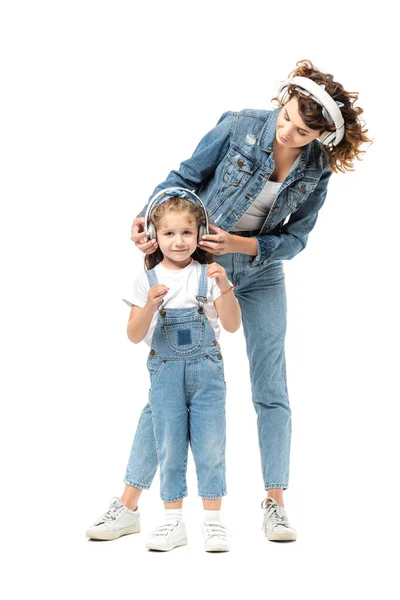 Madre e figlia in abiti denim ascoltare musica in cuffie isolate su bianco — Foto stock