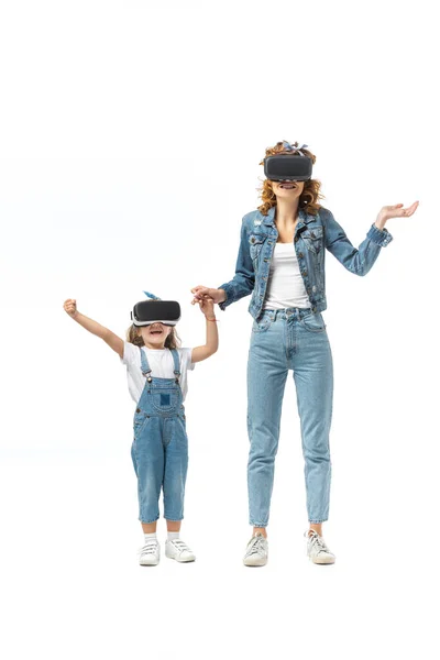 Мать и дочь в джинсовых нарядах и наушниках виртуальной реальности держатся за руки изолированные на белом — стоковое фото