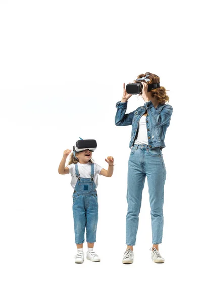 Madre e hija en trajes de mezclilla y auriculares de realidad virtual aislados en blanco - foto de stock