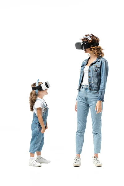 Мать и дочь в джинсовых нарядах и гарнитурах виртуальной реальности смотрят друг на друга изолированно на белом — стоковое фото