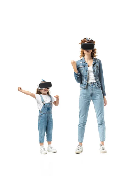 Madre e hija en trajes de mezclilla y auriculares de realidad virtual gestos aislados en blanco - foto de stock