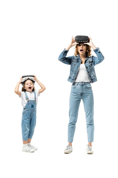 Shocked mother and daughter in denim outfits and virtual reality headsets isolated on white — Stock Photo