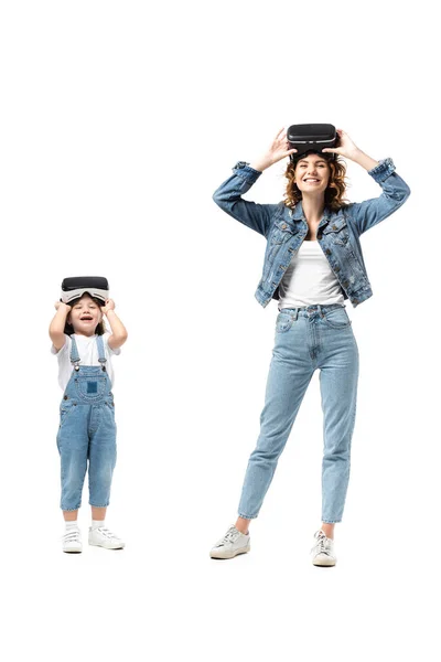 Мать и дочь в джинсовых нарядах и наушниках виртуальной реальности улыбаются изолированно на белом — стоковое фото