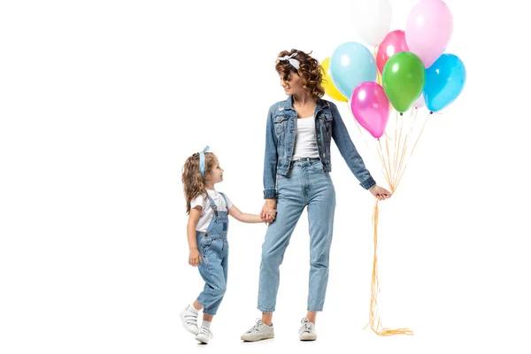 Madre e figlia in abiti in denim con palloncini colorati che tengono le mani isolate su bianco — Foto stock