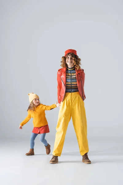 Madre e hija en trajes coloridos rojos y amarillos sobre fondo gris - foto de stock
