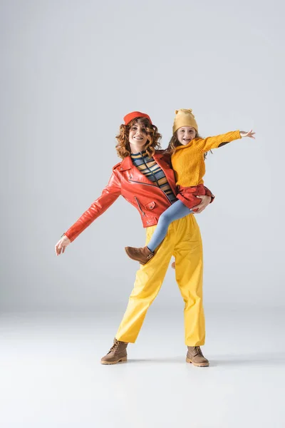 Mother and daughter in colorful red and yellow outfits on grey background — Stock Photo