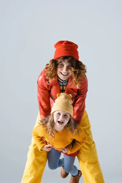 Madre e hija en trajes coloridos rojos y amarillos sonriendo aisladas en gris - foto de stock