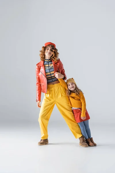 Madre e figlia in abiti colorati rossi e gialli in posa su sfondo grigio — Foto stock