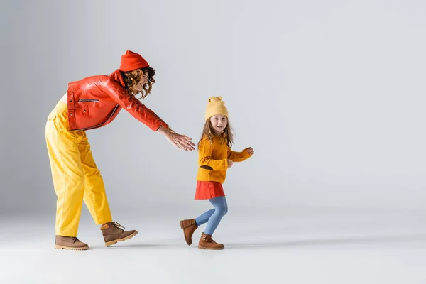 Side view of mother and daughter in colorful red and yellow outfits running on grey background — Stock Photo