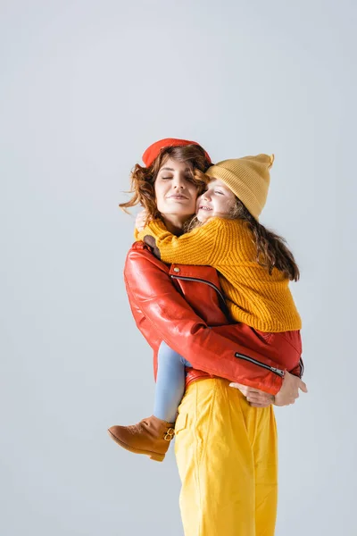 Mother and daughter in colorful red and yellow outfits embracing isolated on grey — Stock Photo