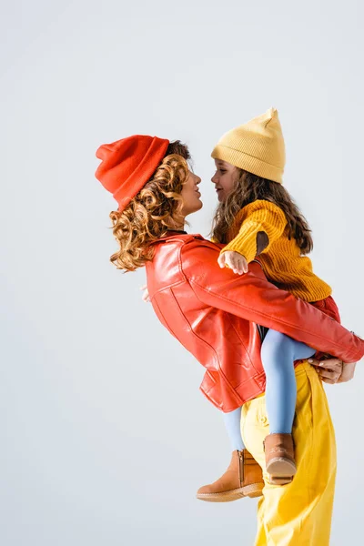 Seitenansicht der Mutter in buntem rot-gelbem Outfit, die Tochter isoliert auf grau hält — Stockfoto