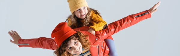 Mère en tenue rouge et jaune colorée imitant avion avec fille sur le dos isolé sur gris, prise de vue panoramique — Photo de stock