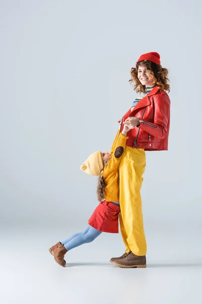 Side view of mother and daughter in colorful red and yellow outfits playing on grey background — Stock Photo