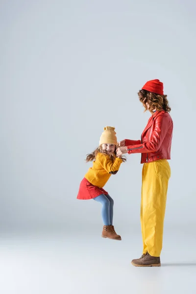 Vista laterale di madre e figlia in abiti colorati rossi e gialli che giocano su sfondo grigio — Foto stock