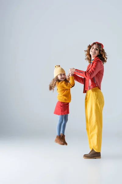 Vista lateral de la madre y la hija en trajes coloridos rojos y amarillos jugando sobre fondo gris - foto de stock