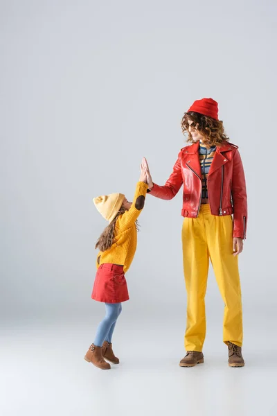 Mutter und Tochter in bunten roten und gelben Outfits geben High Five auf grauem Hintergrund — Stockfoto