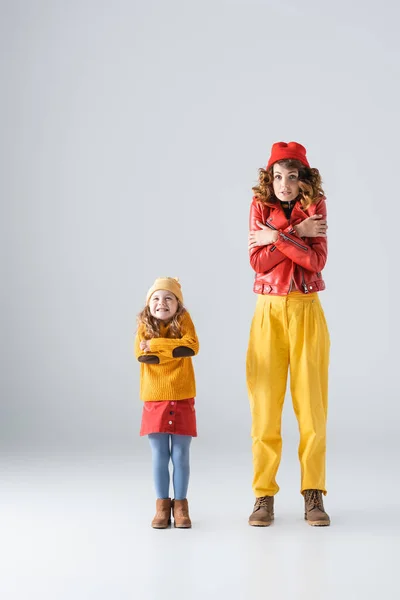 Мати і дочка в барвистих червоних і жовтих вбраннях відчувають холод на сірому фоні — стокове фото