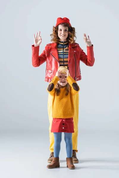 Mother and daughter in colorful red and yellow outfits showing ok signs on grey background — Stock Photo