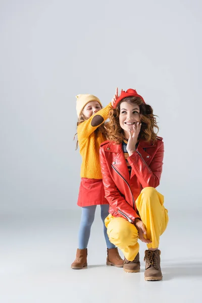 Mutter und Tochter in bunten roten und gelben Outfits amüsieren sich auf grauem Hintergrund — Stockfoto