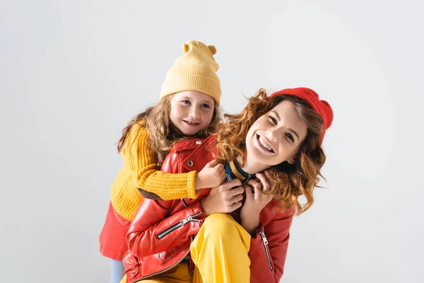 Madre e hija en coloridos trajes rojos y amarillos abrazándose aisladas en gris - foto de stock
